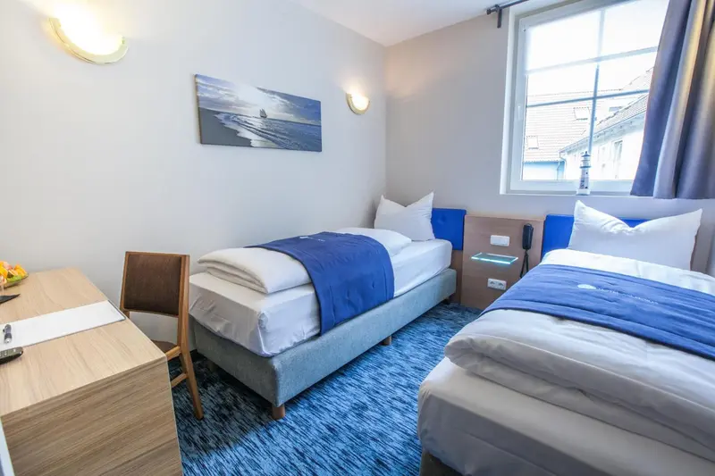 Une chambre avec deux lits simples et un bureau.