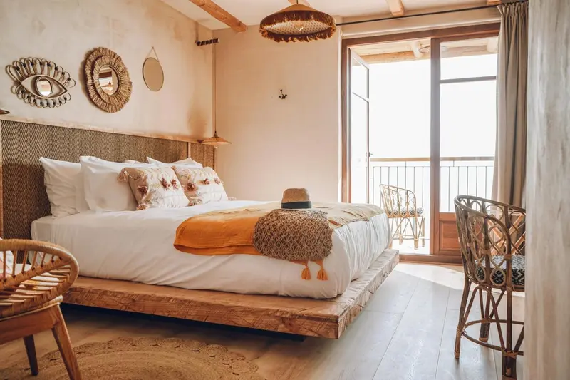 Une chambre lumineuse avec un grand lit recouvert de textiles colorés et un accès à une terrasse.