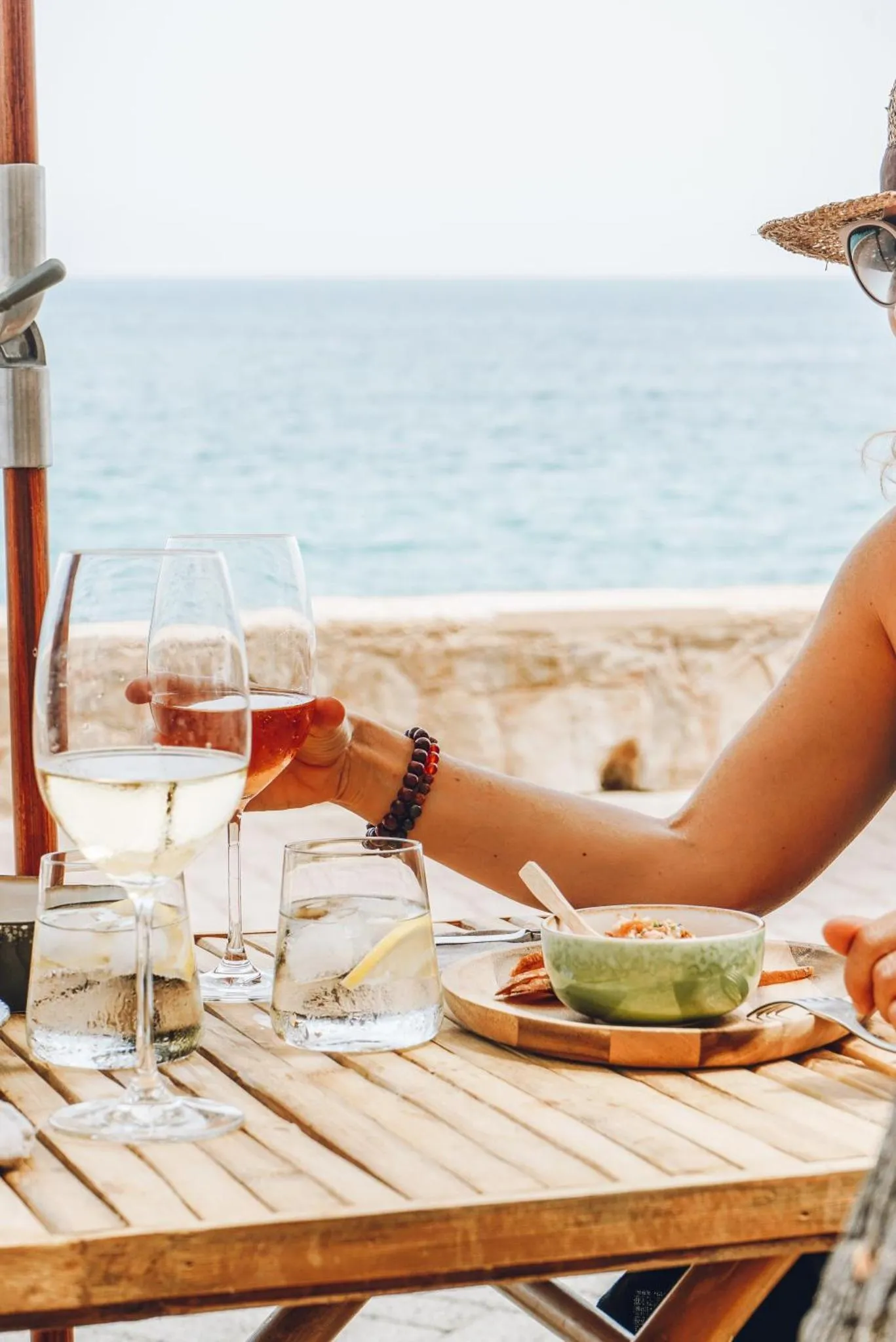 Une table en bois avec des verres et de la nourriture en bord de mer.