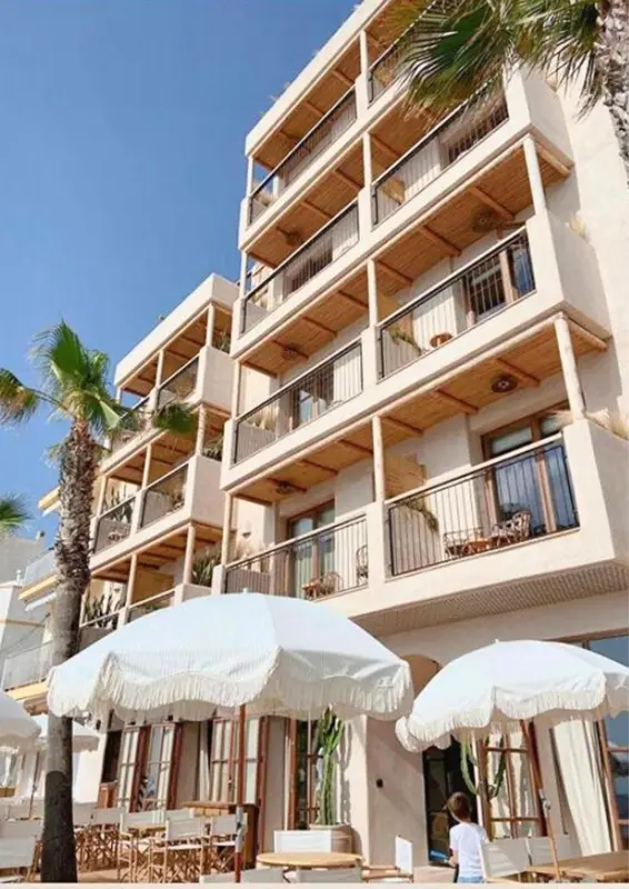 Façade d'un bâtiment beige à plusieurs étages avec des balcons et des parasols blancs.