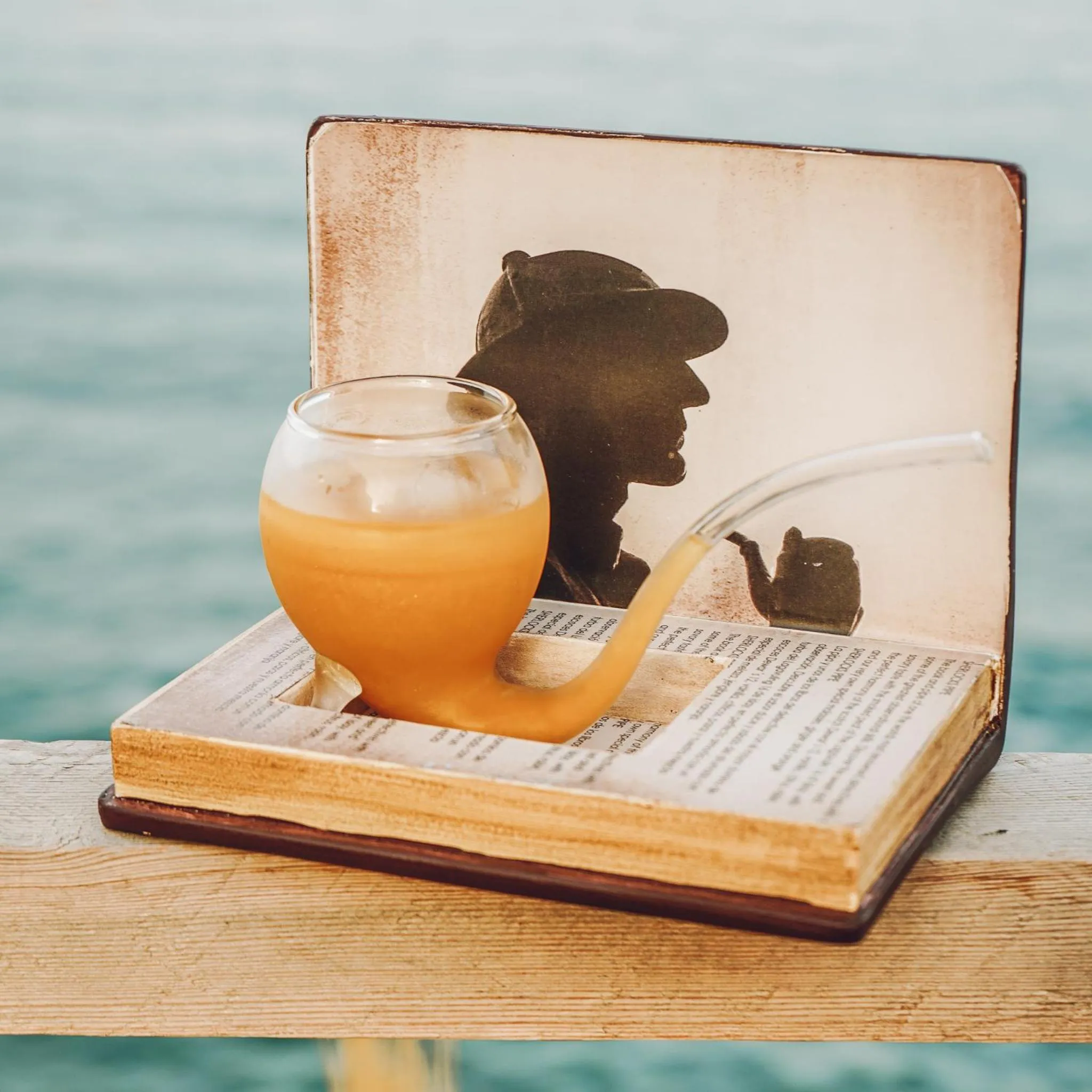 Un verre de boisson est posé sur un livre ouvert en bord de mer.