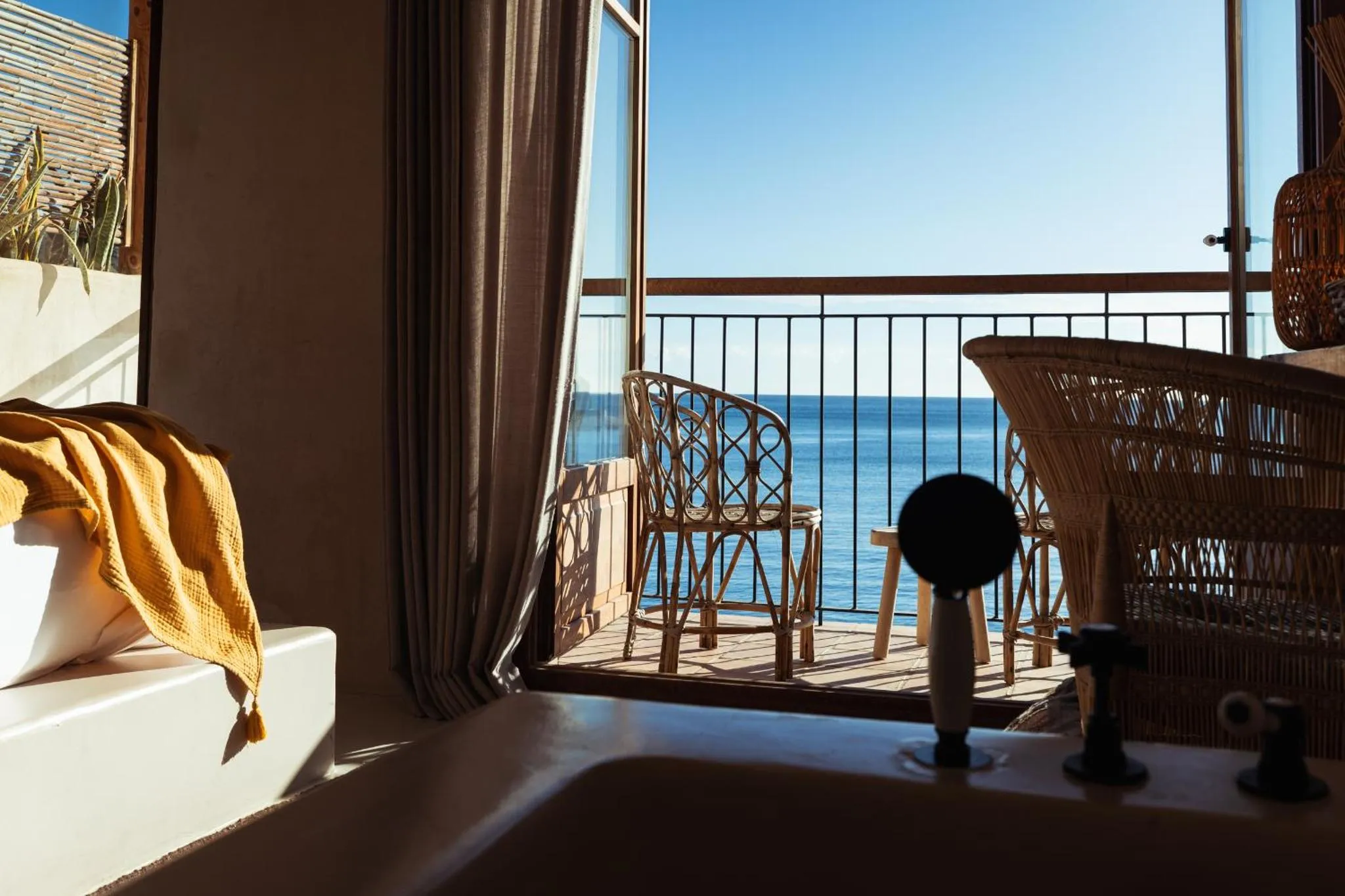 Vue sur la mer depuis un balcon aménagé avec des fauteuils en osier.