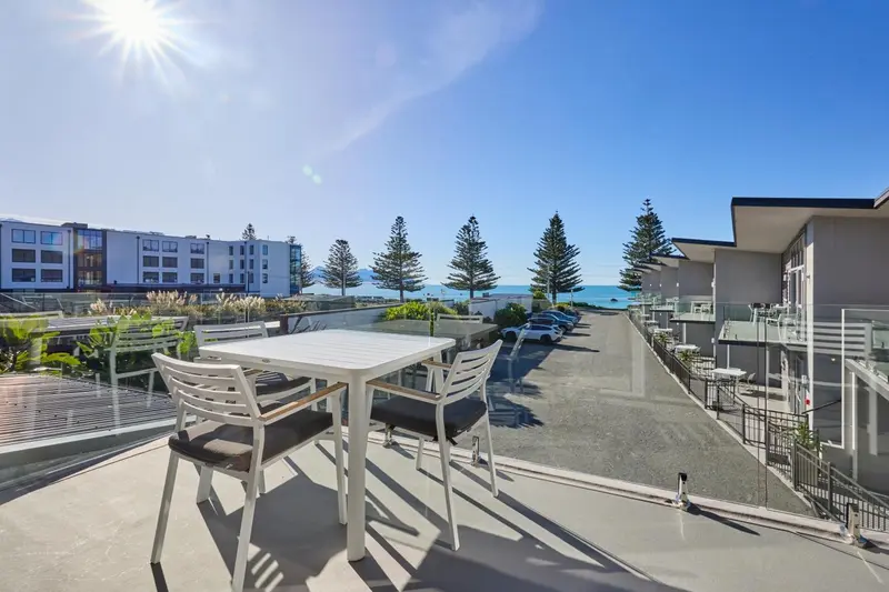 Terrasse aménagée avec table et chaises donnant sur un parking et la mer.