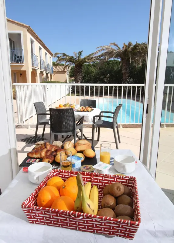Une table de petit-déjeuner est dressée sur une terrasse ensoleillée.