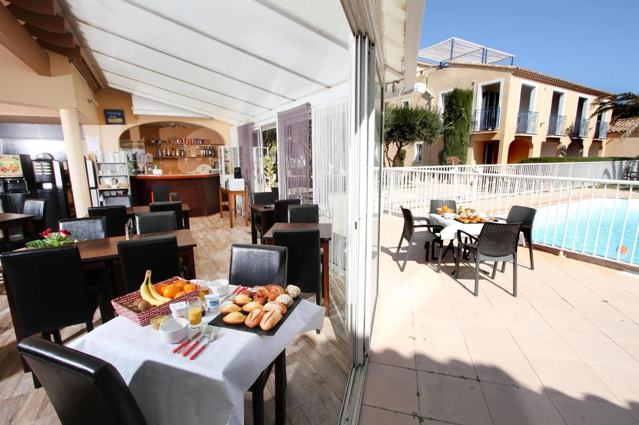 Une table est dressée avec un petit-déjeuner sur une terrasse ensoleillée près d'une piscine.