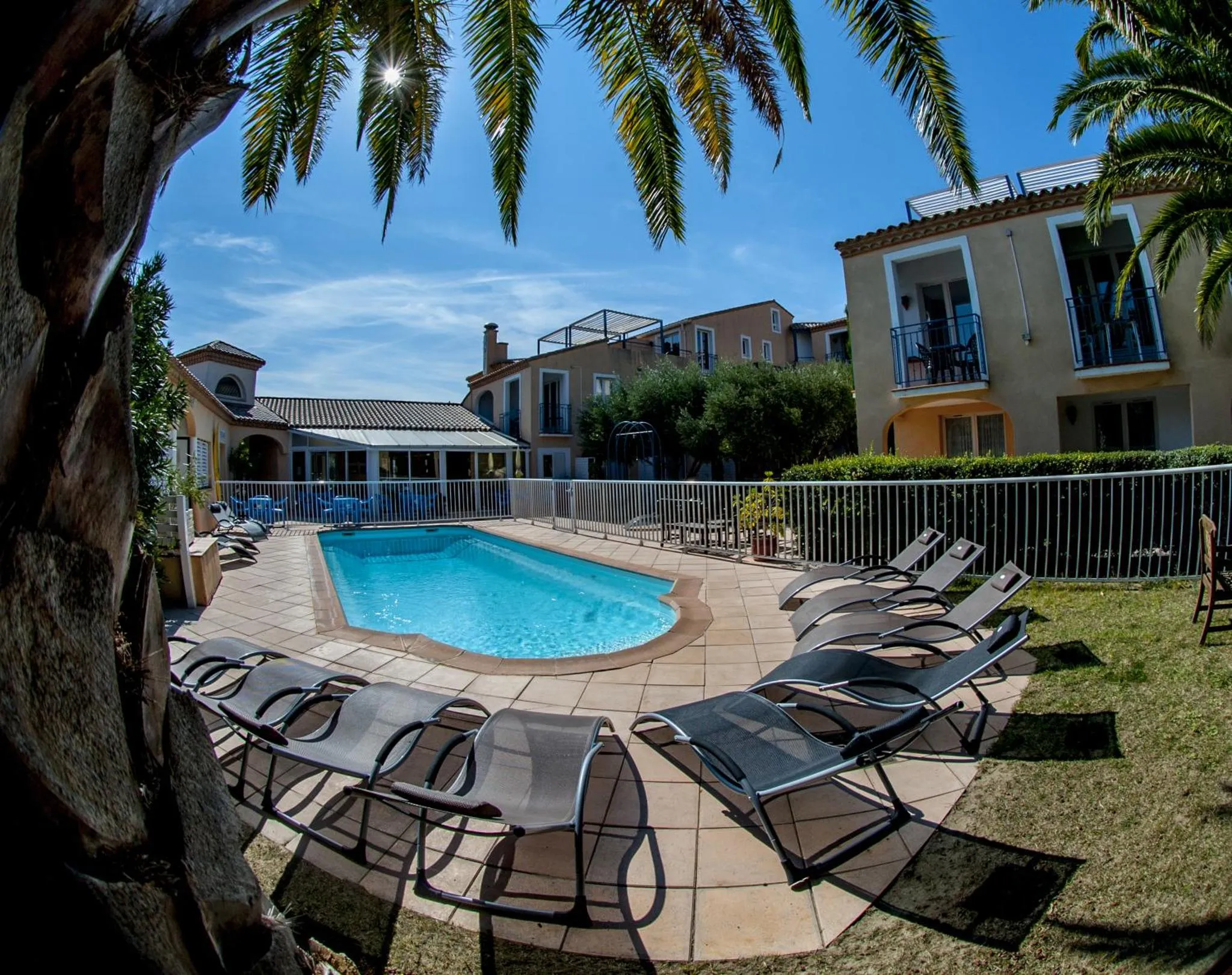 Transats alignés autour d'une piscine ensoleillée, avec un bâtiment en arrière-plan.