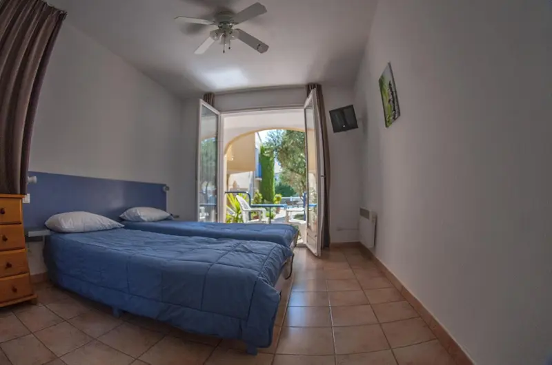 Chambre avec deux lits simples donnant sur une terrasse ensoleillée.