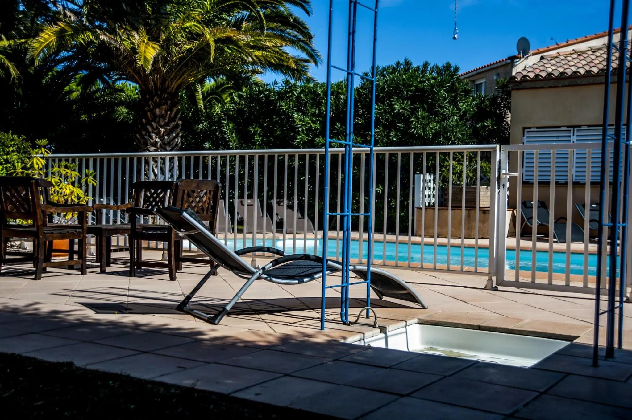 Transats et mobilier de jardin au bord d'une piscine ensoleillée.