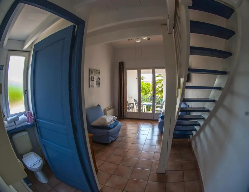 Une piece lumineuse avec un canape bleu et un escalier menant a l'etage.