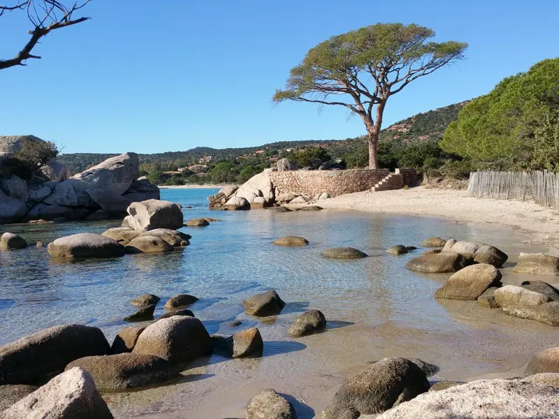 Une plage de sable clair bordée de rochers et d'une eau turquoise.