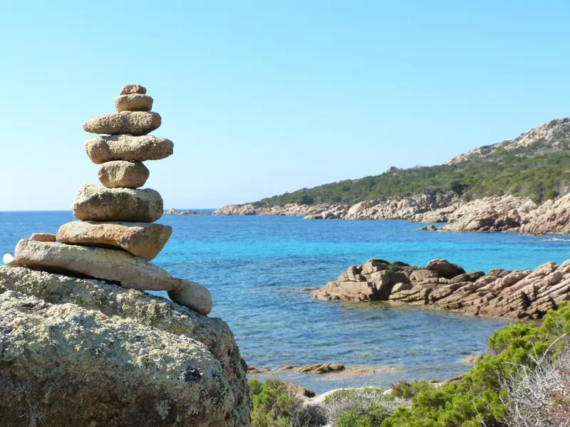 Une pile de pierres se dresse au premier plan, avec une côte rocheuse et la mer en arrière-plan.
