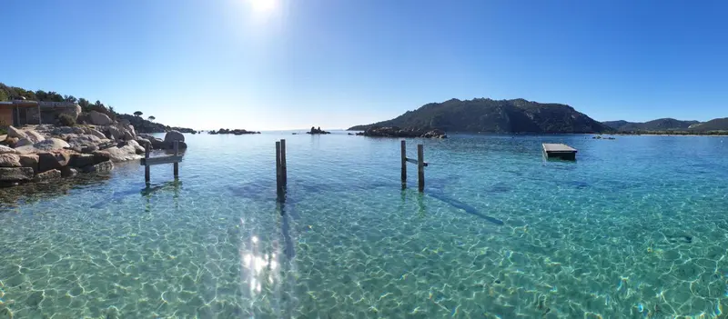 Vue panoramique sur une eau turquoise et une côte rocheuse ensoleillée.