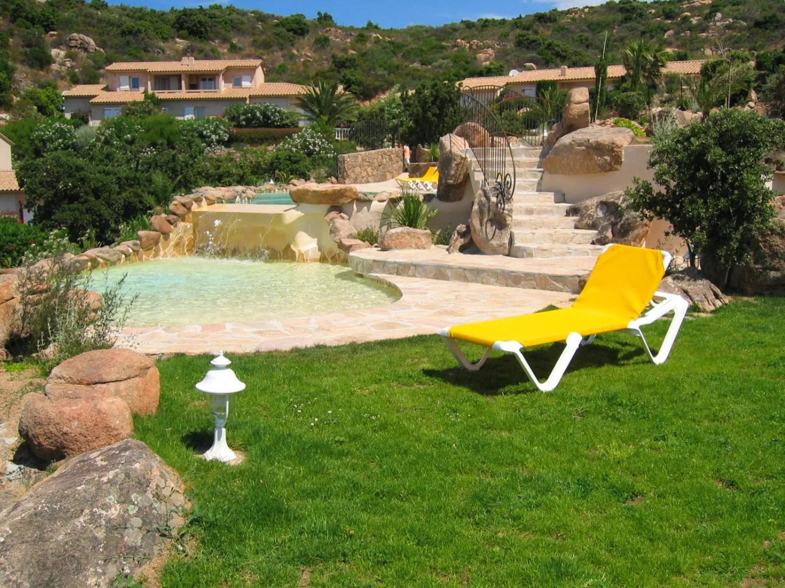 Transats blancs sur une pelouse verte près d'une piscine rocheuse.