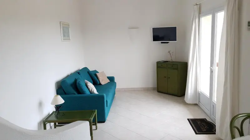 Un salon lumineux avec un canapé bleu turquoise et une commode verte.