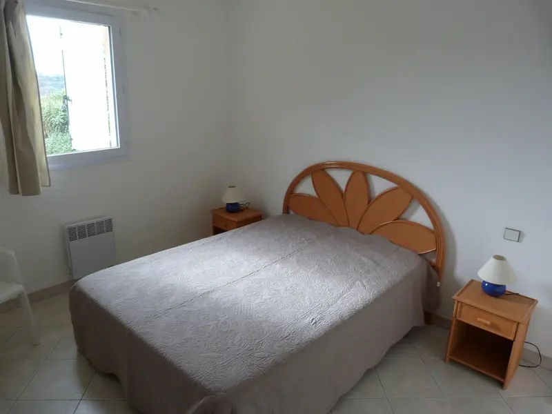 Une chambre lumineuse avec un lit recouvert d'une couverture claire et deux tables de chevet.