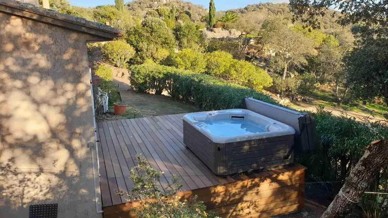 Un jacuzzi extérieur en bois surplombe un jardin verdoyant.
