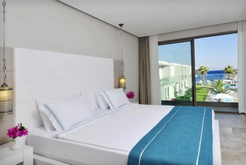 Une chambre lumineuse avec un grand lit face à une baie vitrée donnant sur la mer.