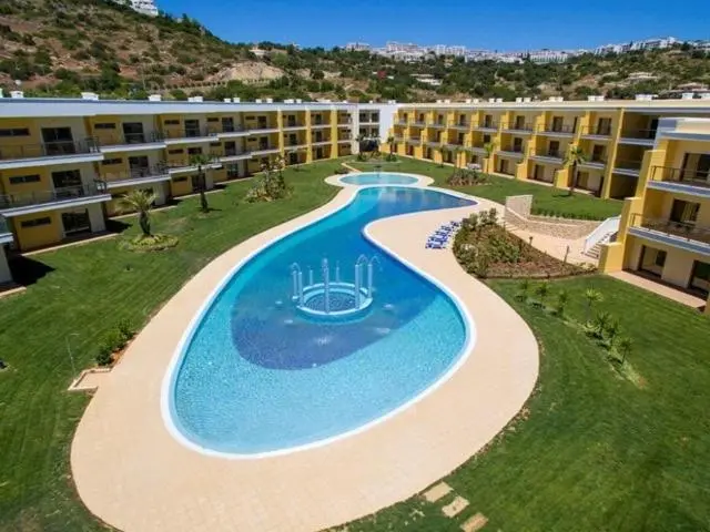 Vue aérienne d'une piscine sinueuse au sein d'un complexe hôtelier jaune et blanc.