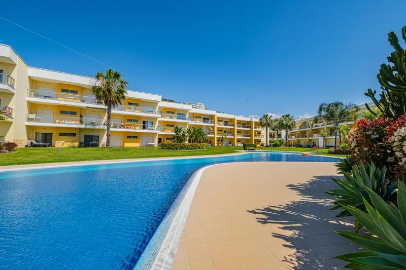 Vue d'une piscine devant un bâtiment jaune avec des balcons.