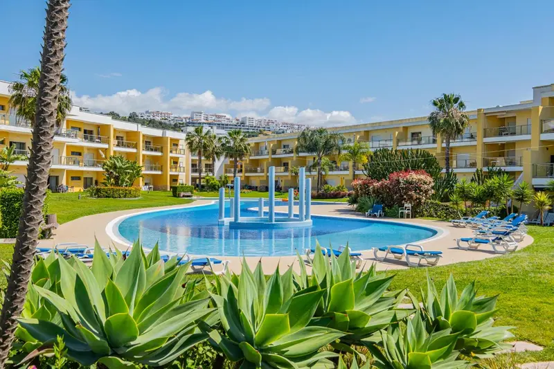 Vue d'une piscine au sein d'un complexe hôtelier jaune et blanc.
