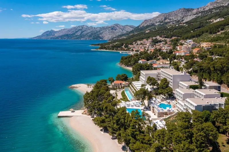 Vue aérienne d'un complexe hôtelier au bord de mer et de montagnes verdoyantes.