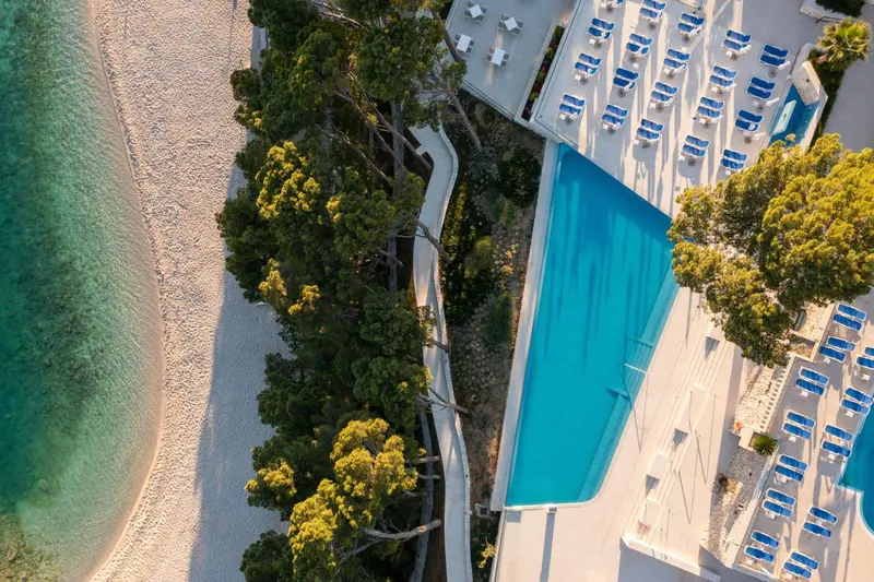 Vue aérienne d'une piscine et d'une plage de sable fin bordée de pins.