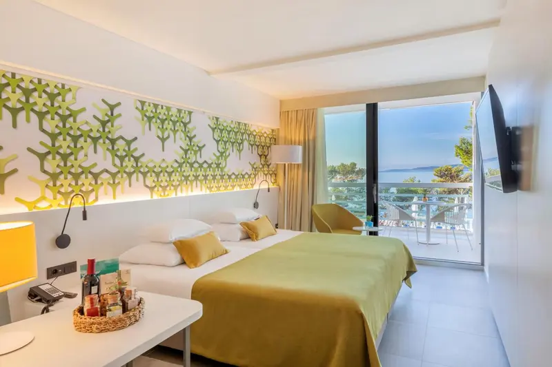 Chambre lumineuse avec un lit fait et une vue sur la mer depuis un balcon.