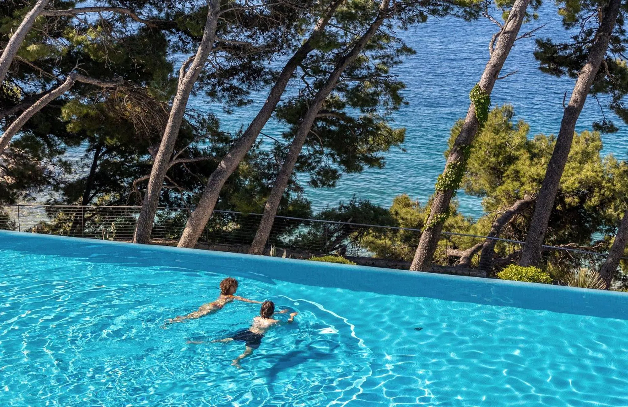 Deux personnes se détendent dans une piscine à débordement avec vue sur la mer.