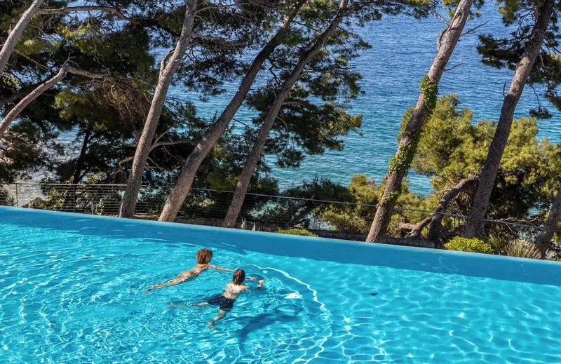 Deux personnes se détendent dans une piscine à débordement avec vue sur la mer.