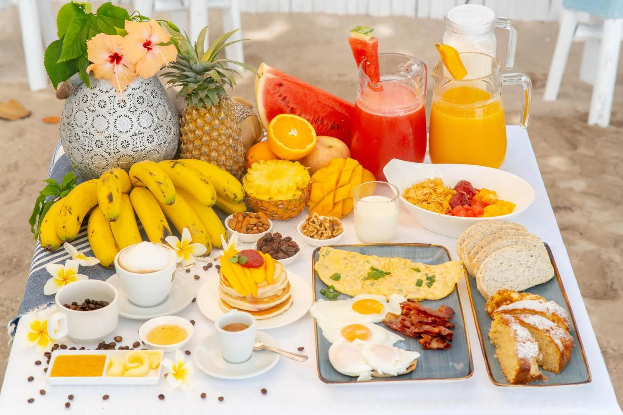 Table basse garnie de fruits frais, de pâtisseries et de boissons sur le sable.