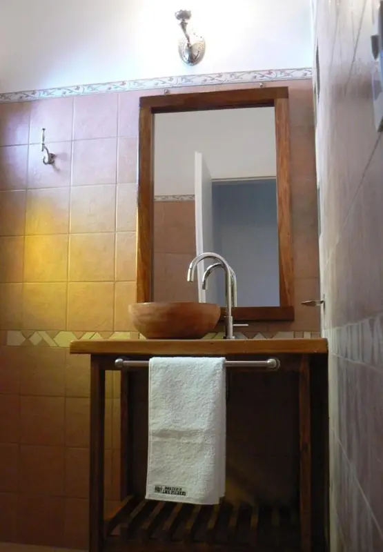 Un lavabo en bois est installé devant un miroir encadré dans une salle de bain carrelée.