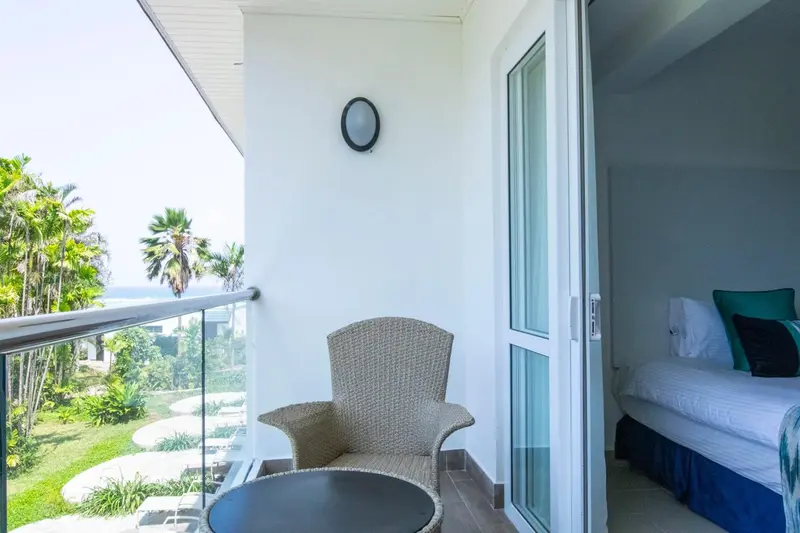 Une terrasse avec un fauteuil et une table donne sur une vue verdoyante et la mer.