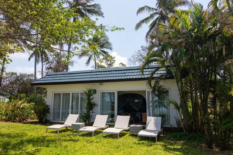 Bâtiment blanc entouré de végétation tropicale avec des chaises longues sur une pelouse.