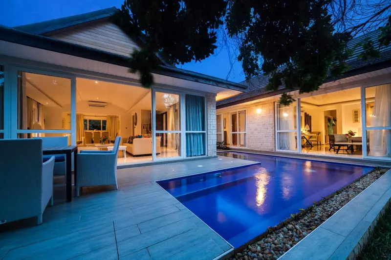 Une piscine illumine une terrasse devant un logement ouvert sur un salon.