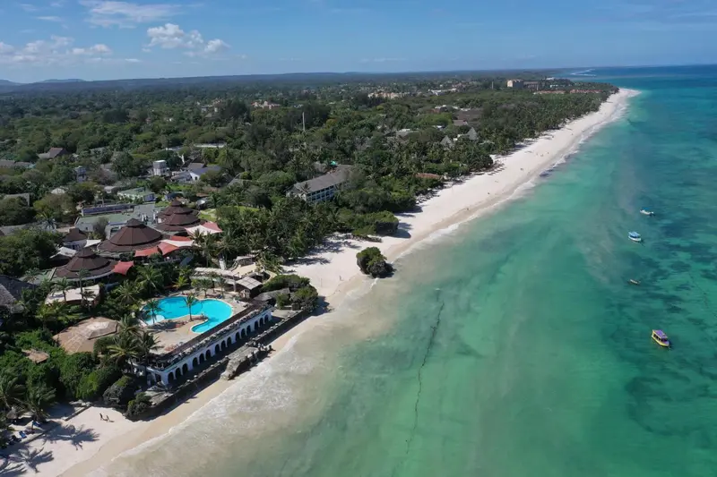 Vue aérienne d'une plage de sable blanc bordée de végétation et d'établissements hôteliers.