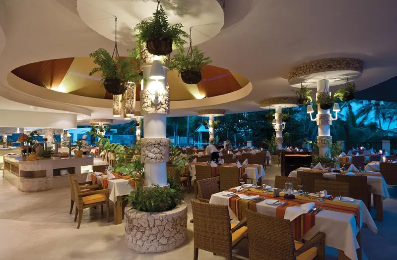 Une salle de restaurant lumineuse avec des tables dressées et une décoration tropicale.