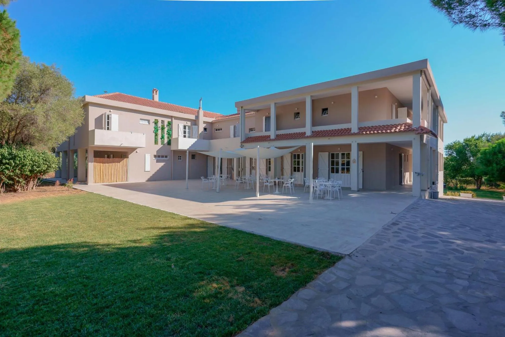 Bâtiment beige avec une terrasse ombragée et une pelouse verdoyante.