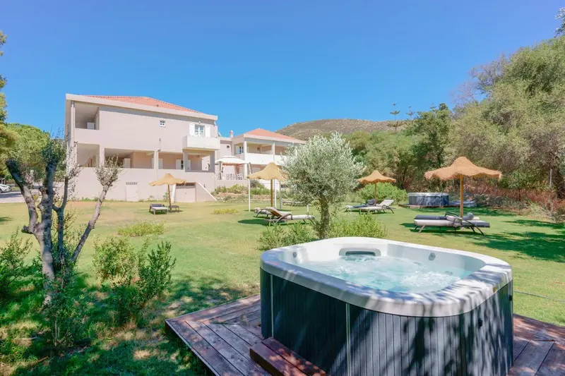 Un jacuzzi au premier plan, avec un bâtiment blanc et une pelouse verdoyante en arrière-plan.