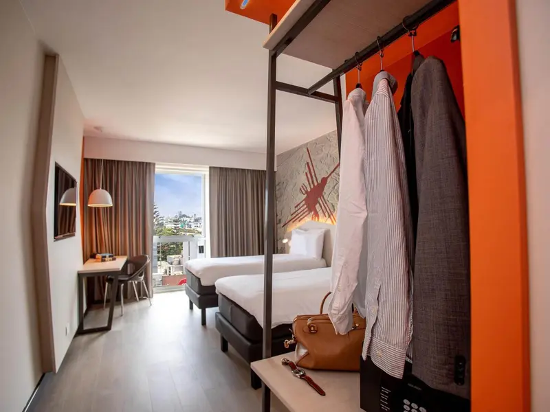 Une chambre lumineuse avec deux lits simples et un espace bureau près d'une fenêtre.