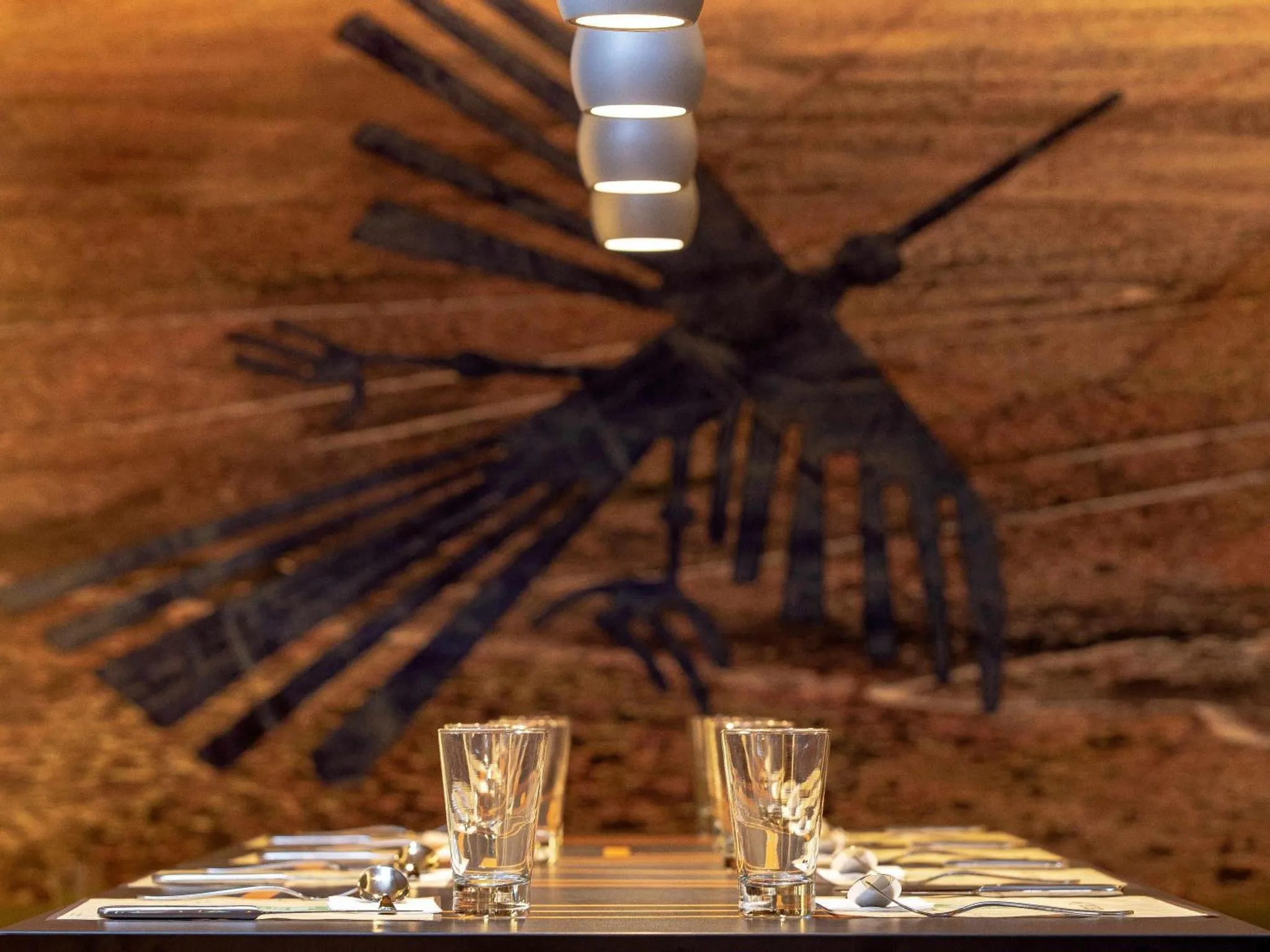 Une table dressée avec des couverts et des verres devant un mur texturé décoré d'une sculpture.