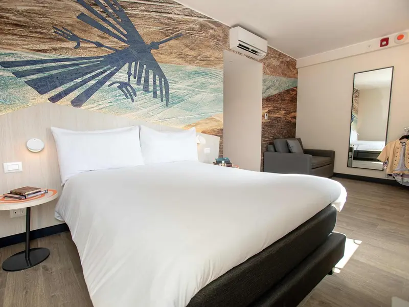 Une chambre lumineuse avec un grand lit et une décoration murale abstraite.