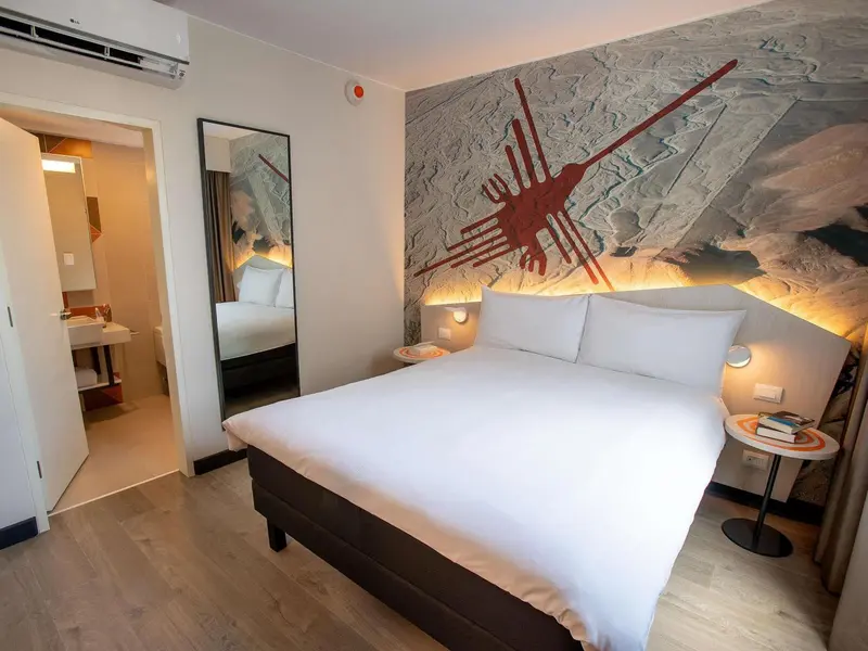 Une chambre lumineuse avec un grand lit et un décor mural abstrait.