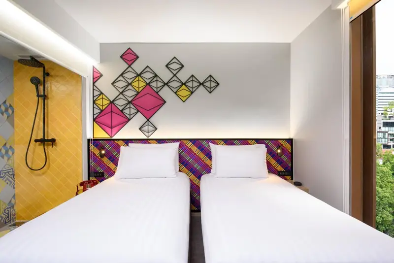 Chambre moderne avec deux lits simples et une décoration murale colorée.
