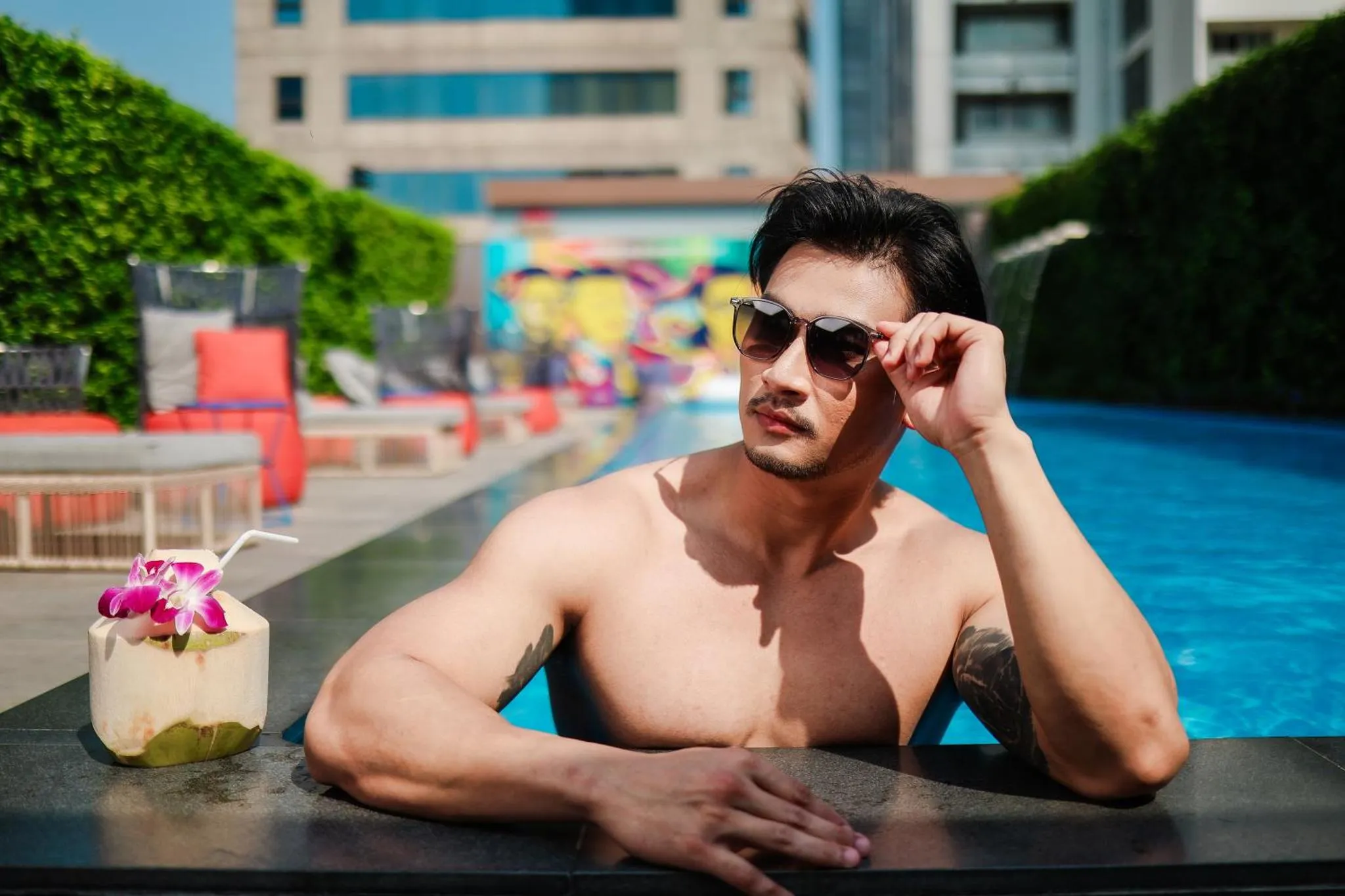 Un homme torse nu se repose au bord d'une piscine ensoleillée avec un cocktail.