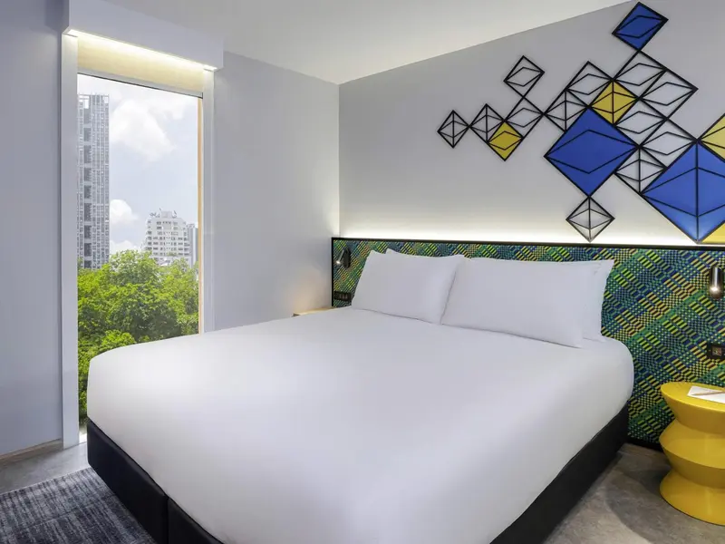 Une chambre lumineuse avec un grand lit et une décoration murale abstraite.