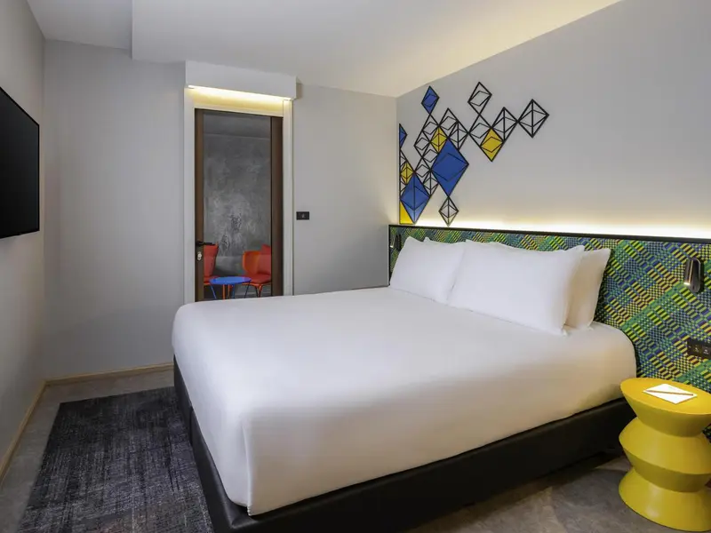 Une chambre lumineuse avec un grand lit et une décoration murale colorée.