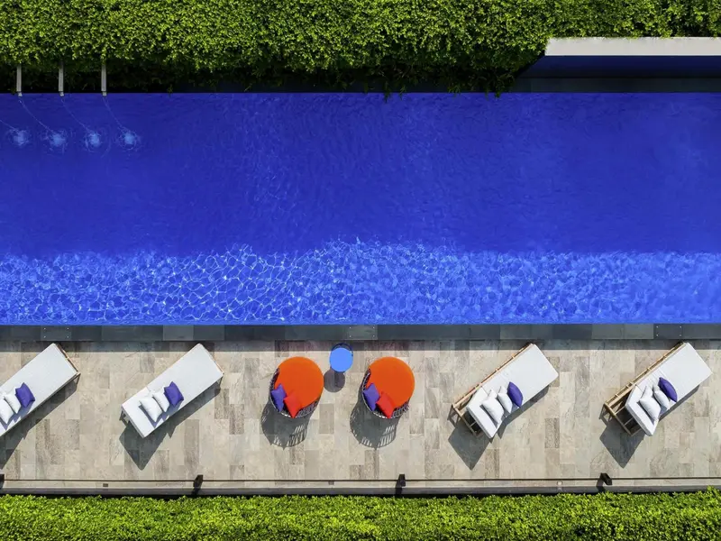 Vue aérienne d'une piscine rectangulaire bordée de chaises longues colorées.
