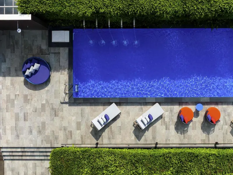 Vue aérienne d'une piscine rectangulaire bordée de chaises longues et de végétation.