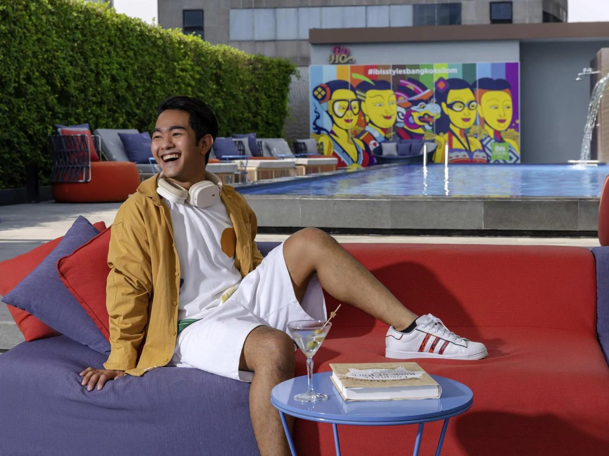 Un homme souriant se détend au bord d'une piscine avec un cocktail.