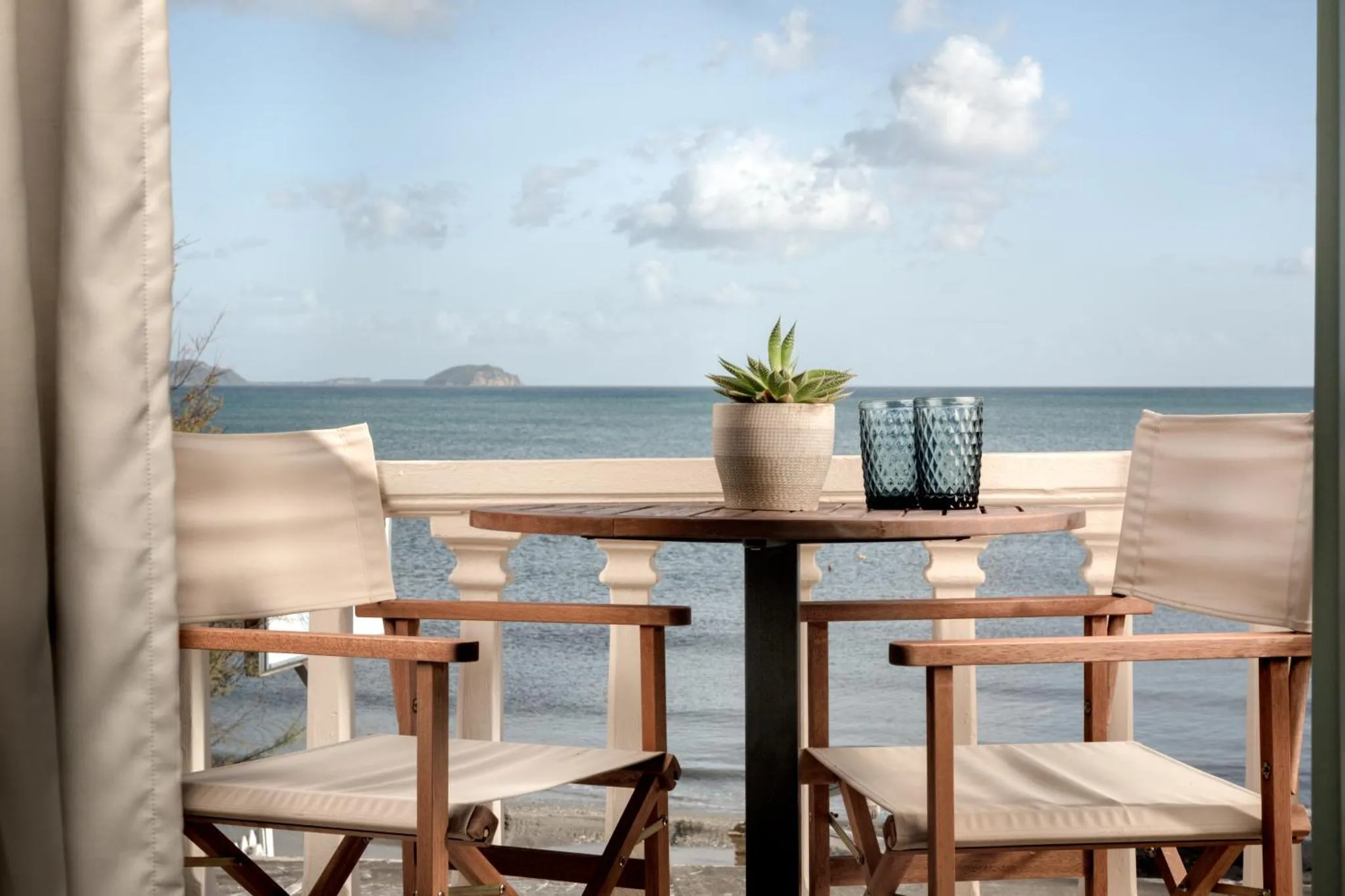 Une table et deux chaises en bois sur une terrasse avec vue sur la mer.